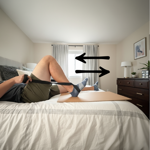 Person with total knee replacement using heel slide board to perform heel slides for knee flexion range of motion. 